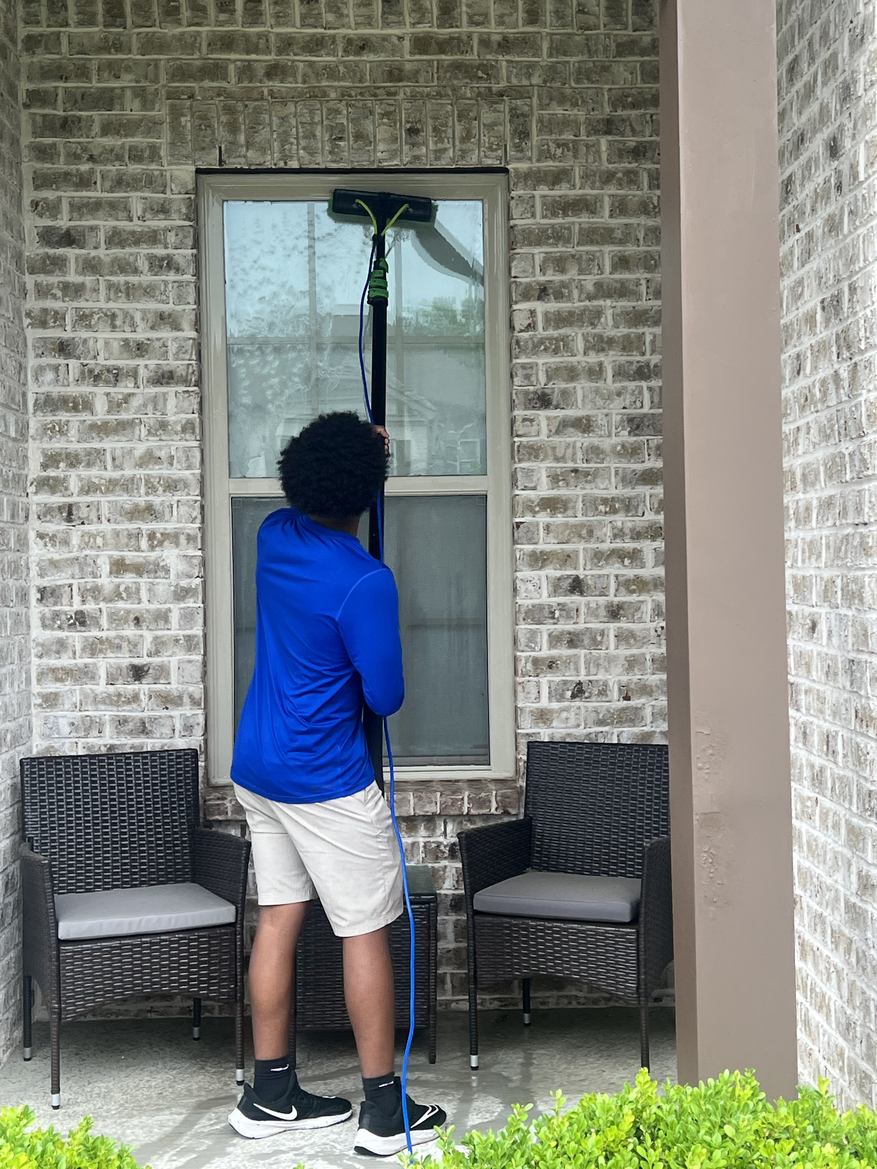 Professional window cleaner using a water-fed pole system on a residential property
